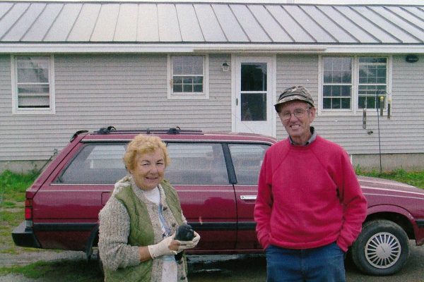 a woman and man standing in front of car parked in front of house