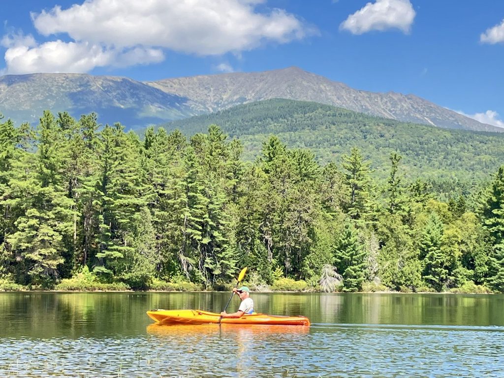 person paddling in yellow kayak with Katahdin in the background