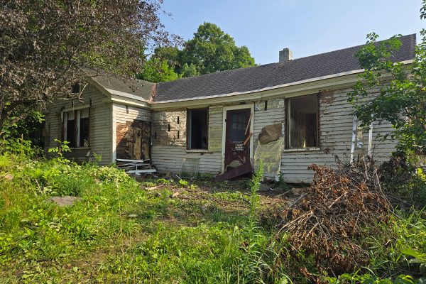 abandoned home deteriorating in grass-covered yard