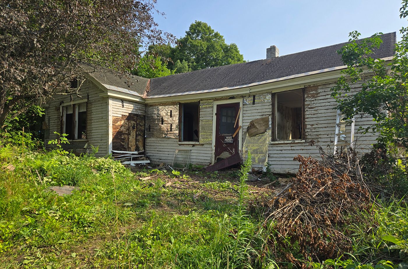 abandoned home deteriorating in grass-covered yard