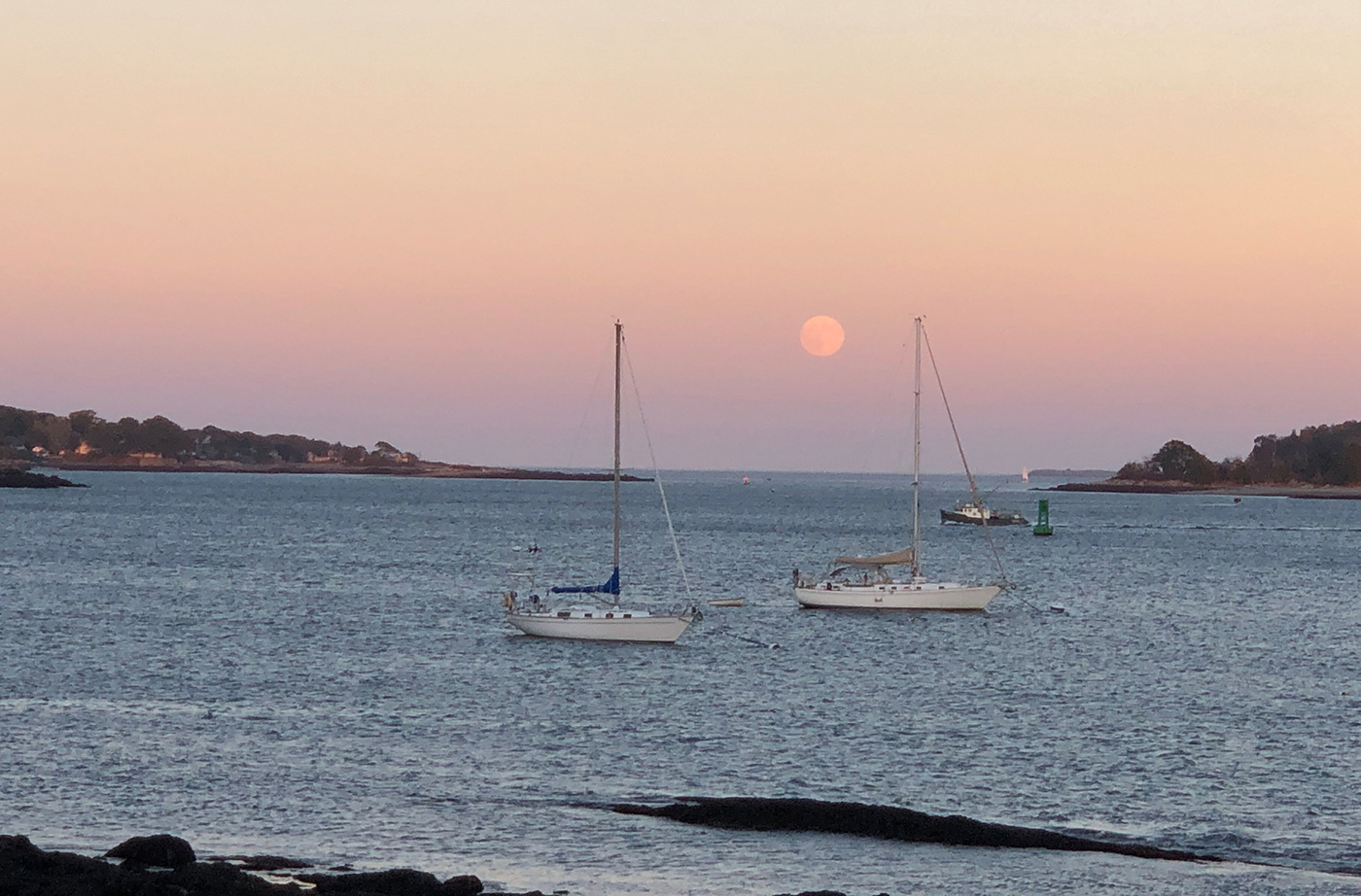 Moon and pink sky over Casco Bay with two boats in foreground
