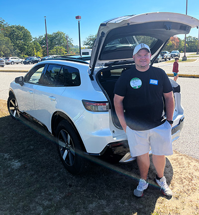 Man in white hat and shorts standing at back of his car with trunk open
