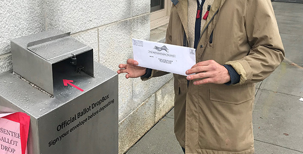 someone holding onto an absentee ballot next to a dropbox