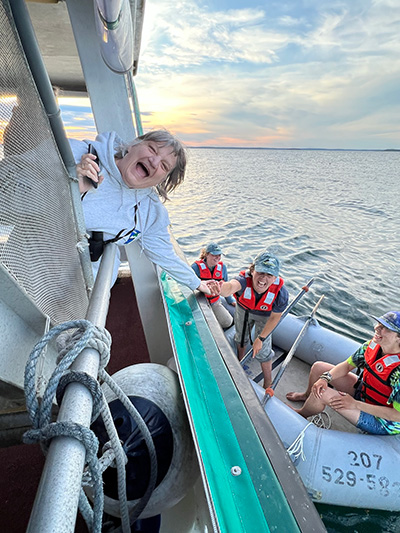 two people smilinig and reaching for each others hands - one from large boat and one on raft