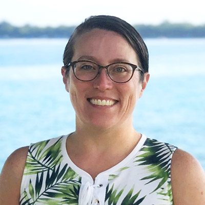 woman wearing glasses smiling with water behind her