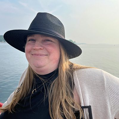 Woman smiling, wearing black hat, in front of water