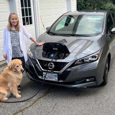 woman and her dog standing next to electric car being charged from home
